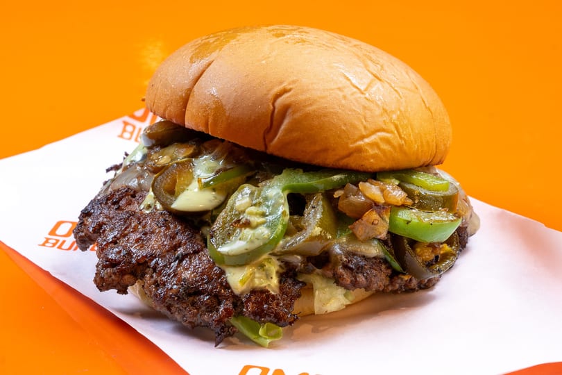 A close-up of a burger with a beef patty, melted cheese, grilled onions, and jalapeños.
