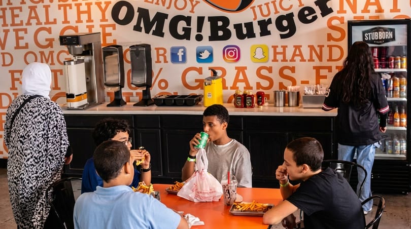 Customers eating burgers and fries at OMG! Burger, with a large branded wall behind them.