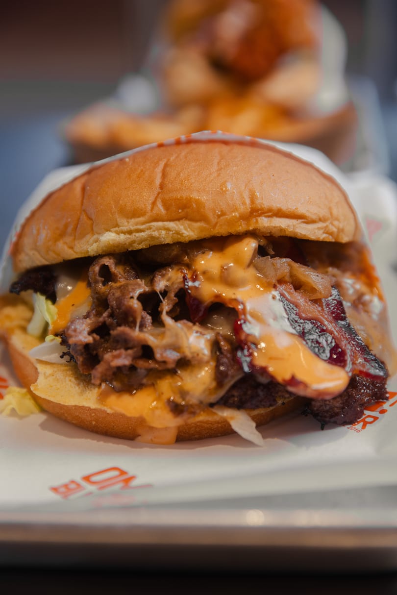 Close-up of a burger with melted cheese, bacon, caramelized onions, and lettuce on a bun.