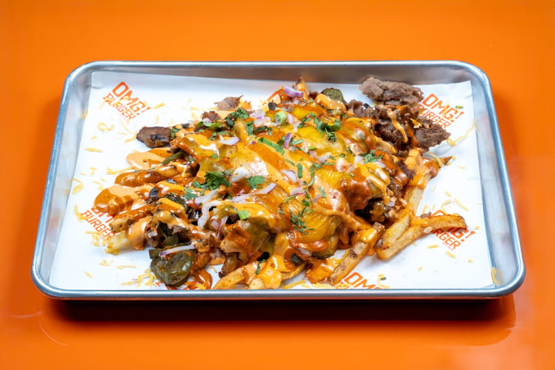OMG! Burger loaded fries with cheese, meat, jalapeños, onions, and sauce on a metal tray.