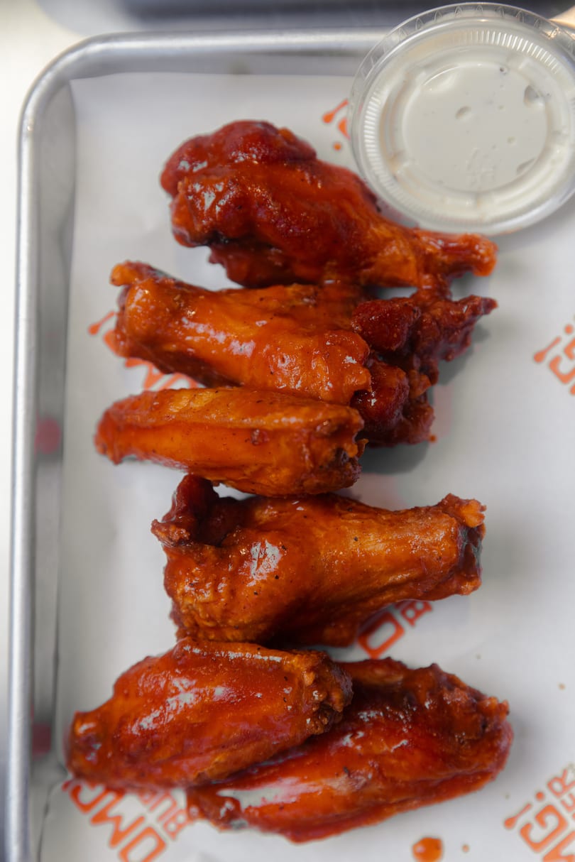 Six buffalo chicken wings with a side of ranch dressing on a metal tray with paper.