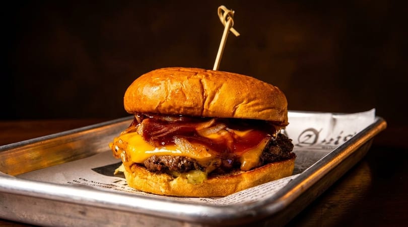 Gourmet burger with melted cheese, caramelized onions, and BBQ sauce on a brioche bun.